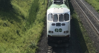 A GO train is traveling along a railway track surrounded by green space. 