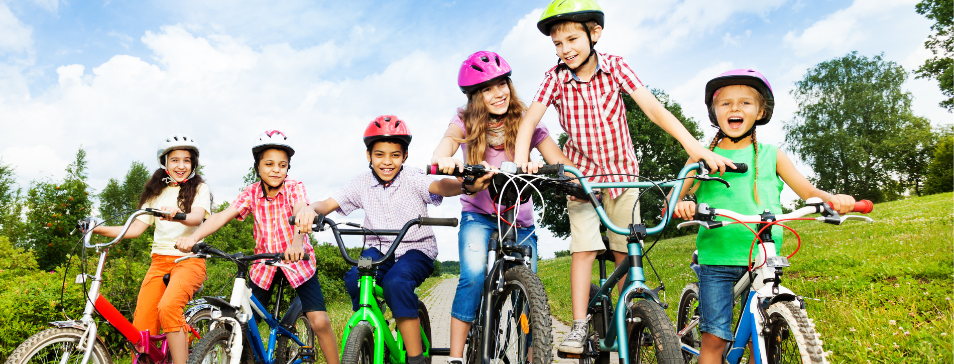 An image of six children sitting on bicycles outside and wearing helmets. 