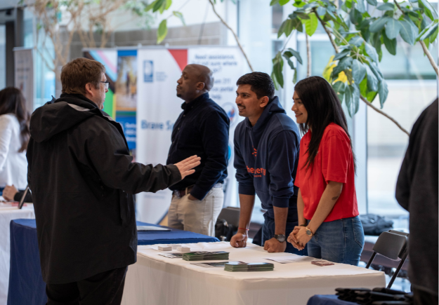 Two people behind a booth speaking to an expo guest. 