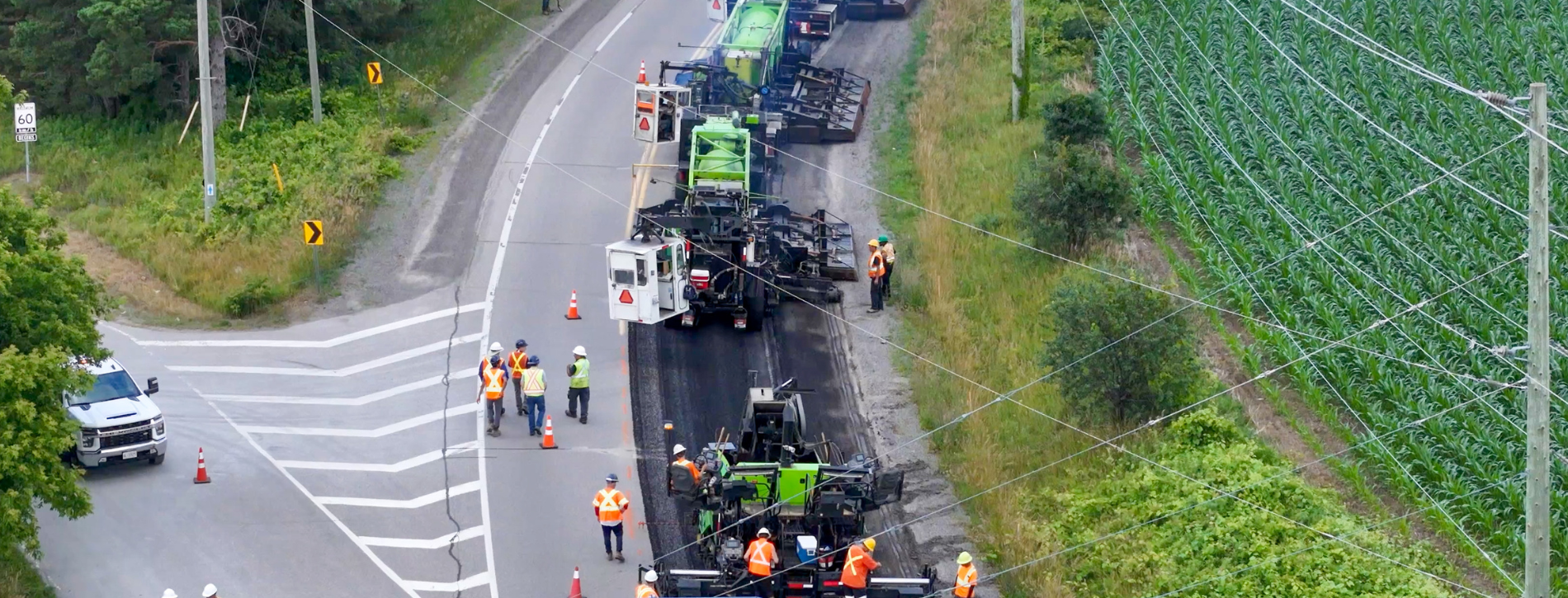 An aerial view of equipment and workers on a road surrounded by trees.