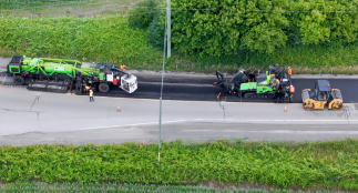 An aerial view of equipment and workers on a road surrounded by trees.
