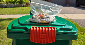 A clear bag with used batteries in it on top of a green bin.