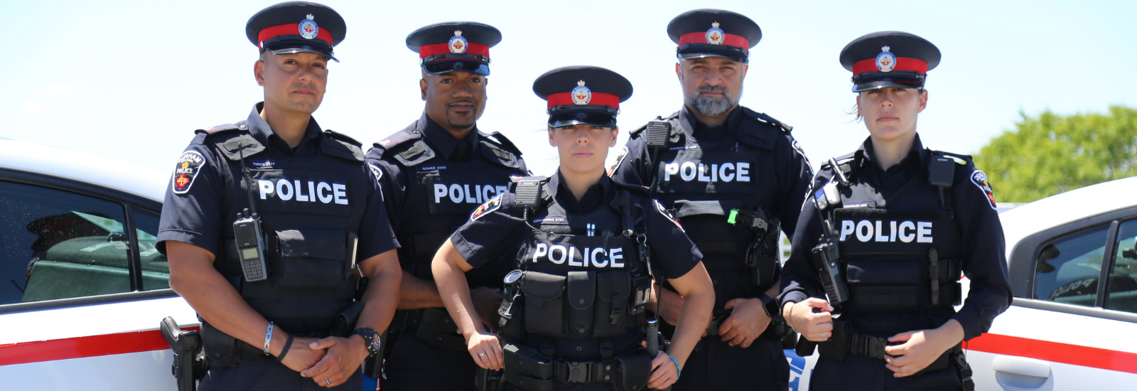 Five police officers standing in front of vehicles