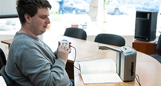 A visually impaired man uses a scanning and reading machine. Link opens a form to request accessible format or communication