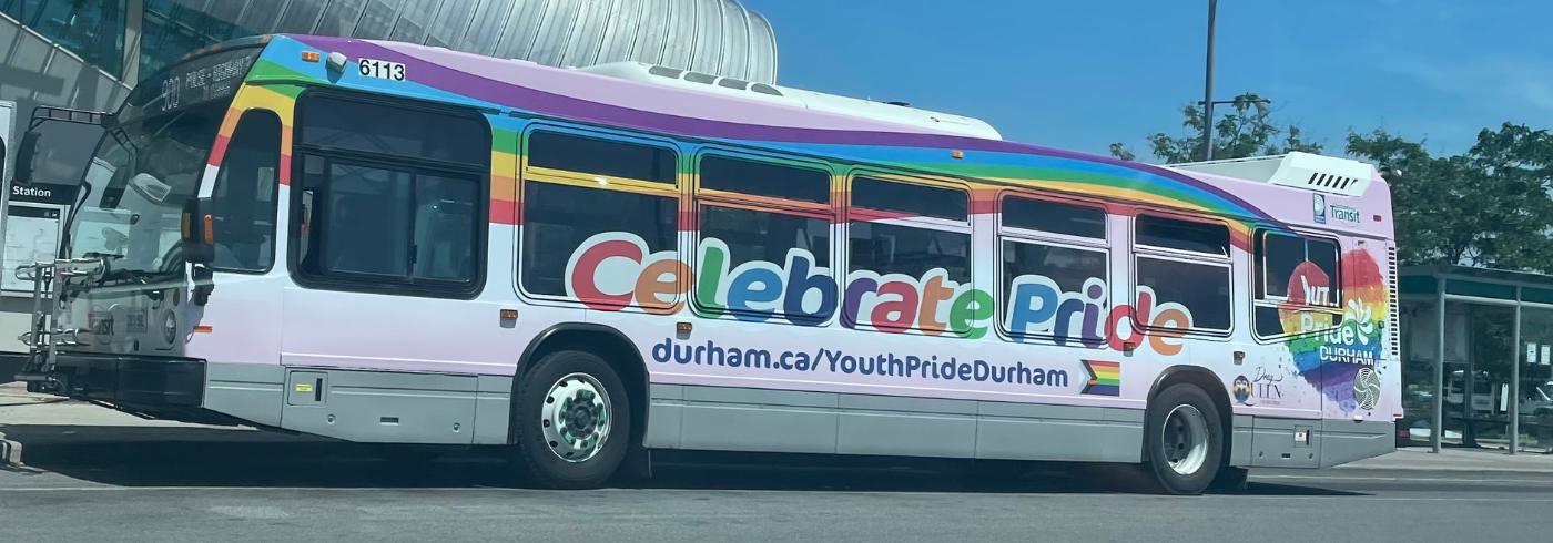 A photo of a bus wrapped with a rainbow. Text across the bus reads Celebrate Pride; durham.ca/YouthPrideDurham