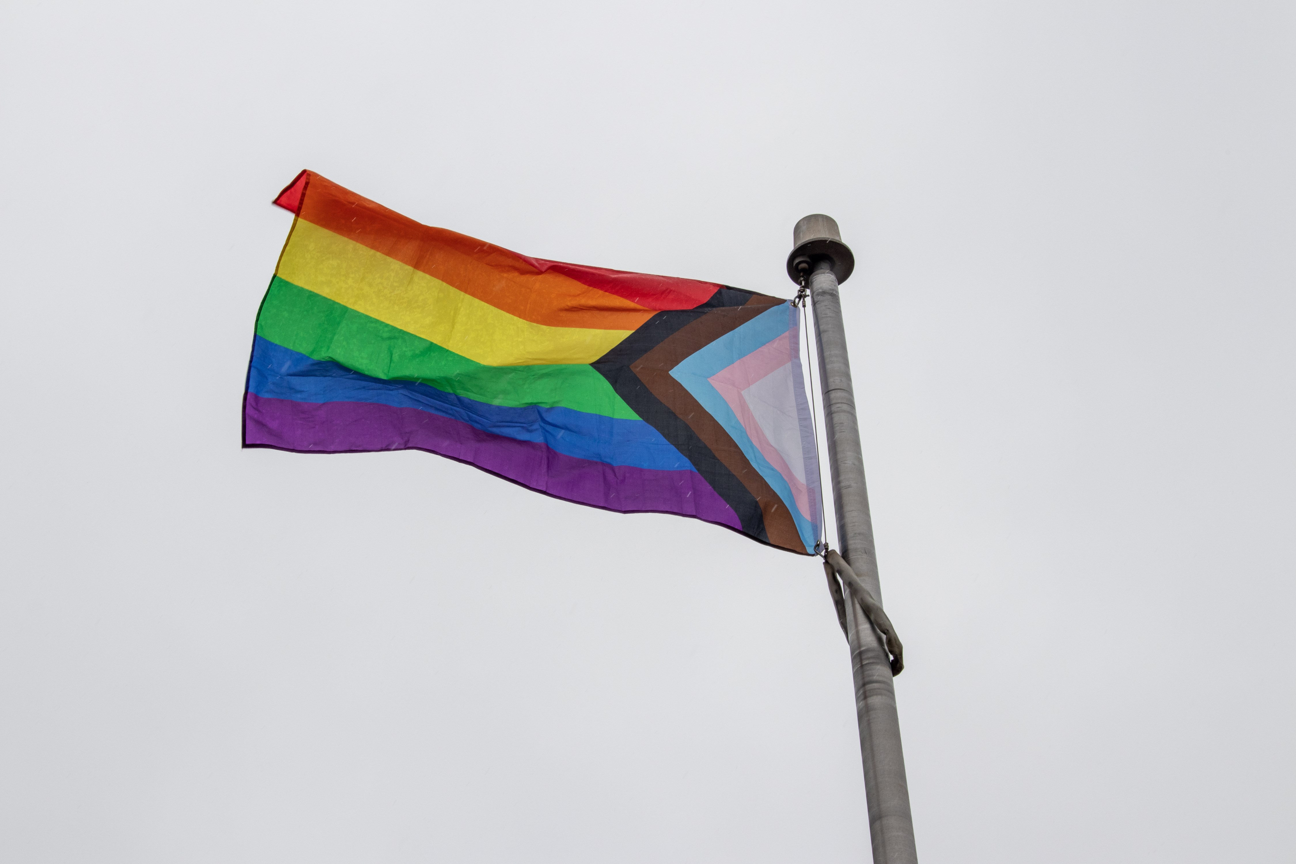 Progressive Pride Flag waving in the wind with a cloudy sky in the background.