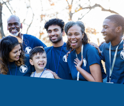 A group of people including adults, youth and a child smiling, outdoors with trees behind them.