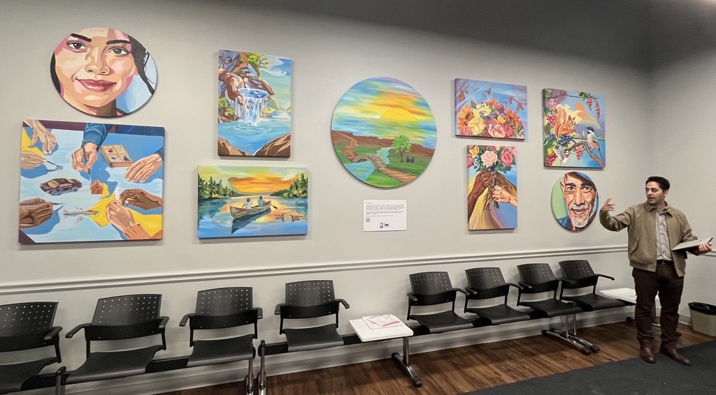 An image of various art pieces on a wall with an artist beside