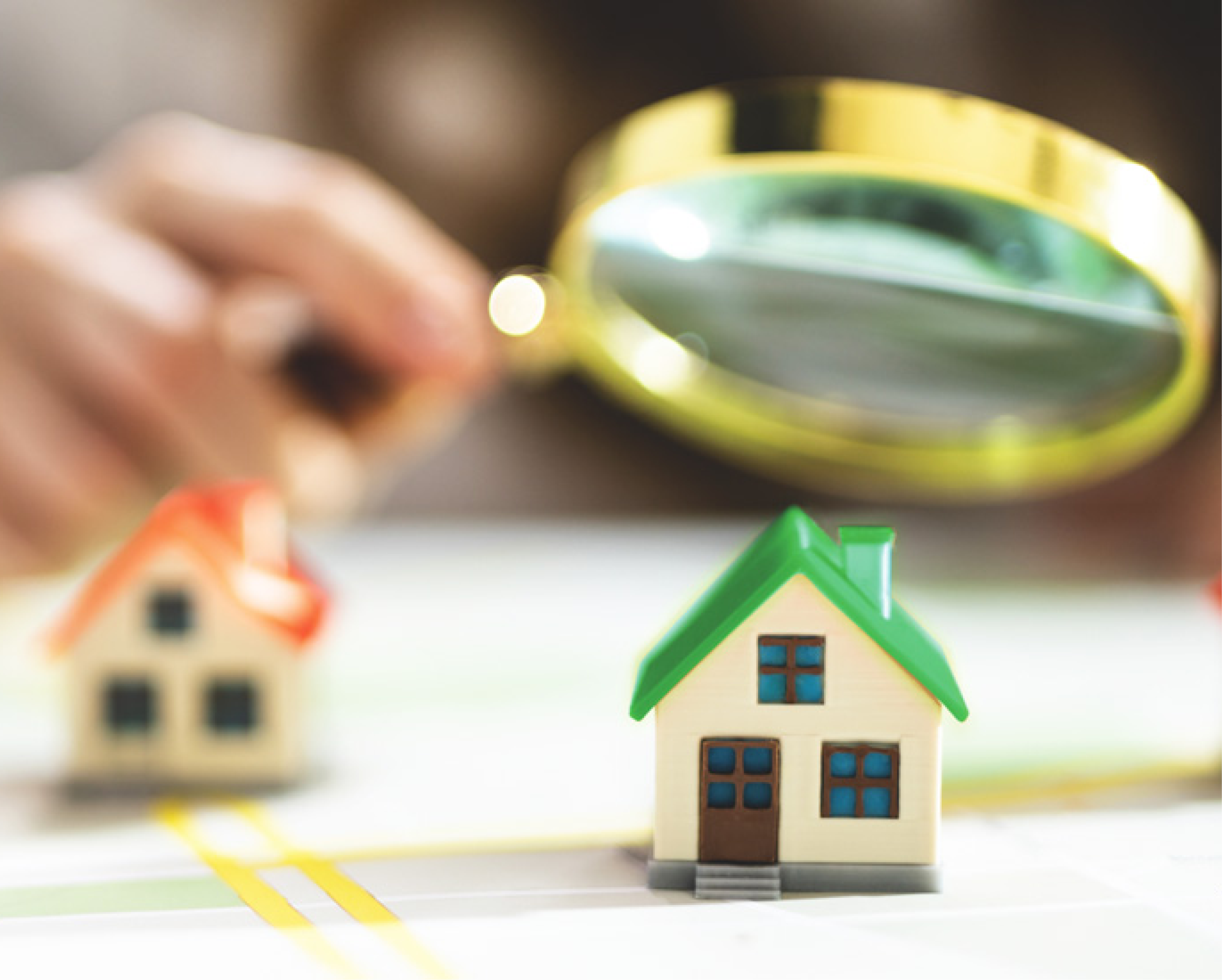 Someone holding a magnifying glass looking at two small model homes.