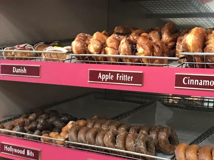 A photo of shelves inside Hollywood Donuts that feature apple fritters amongst other donuts on shelves