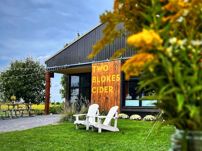 Exterior photo of the Two Blokes Cider tap room, production facility and outdoor patio amongst the apple orchards and fields