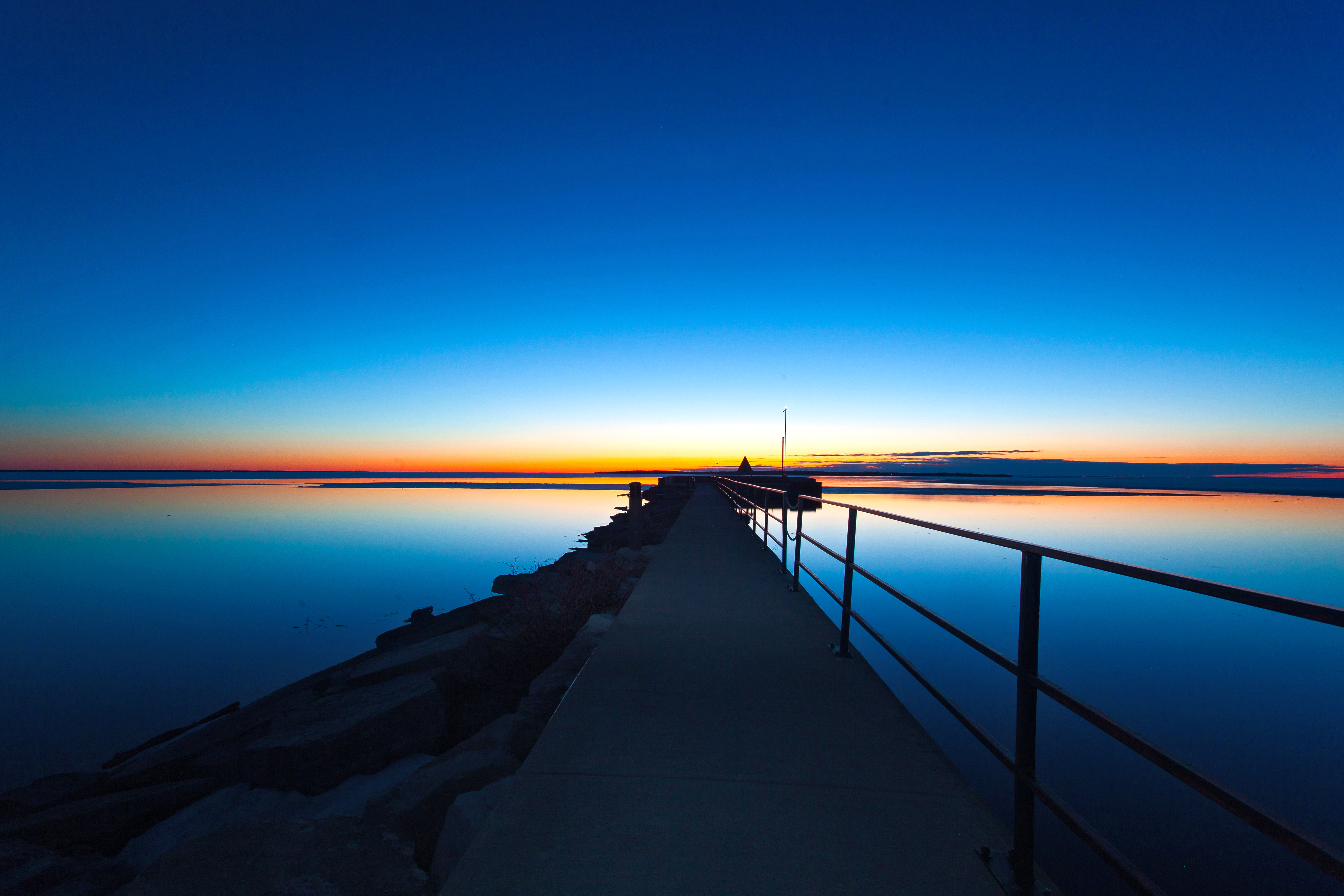 Photo taken on the pier during sunset at the Beaverton Harbour. The water is flat on Lake Simcoe and the sky features vibrant shades of blue, red and orange.