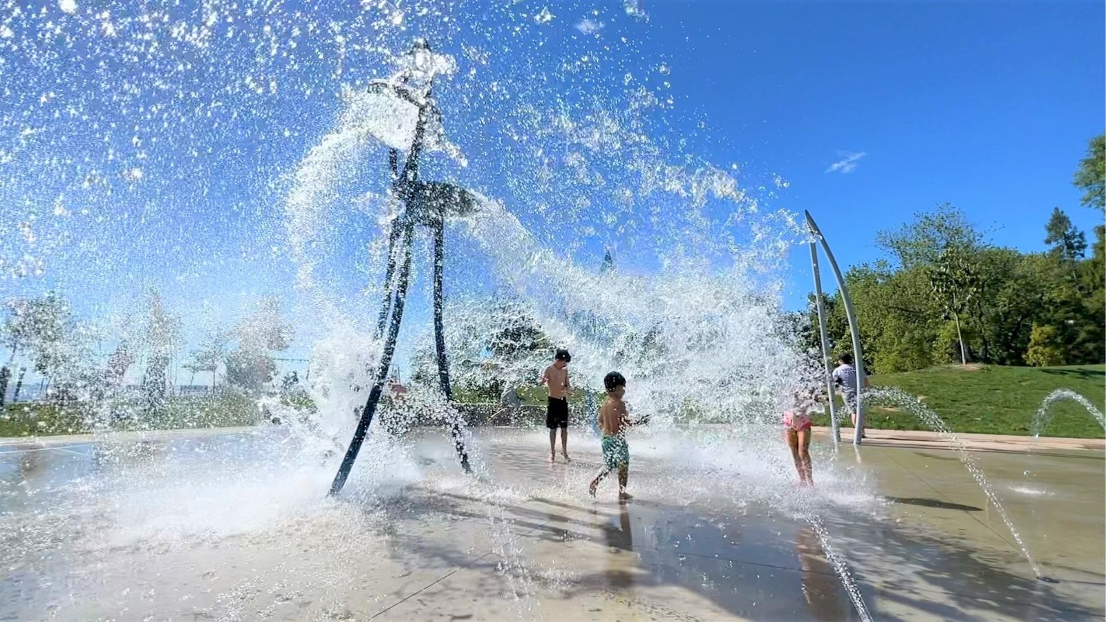 Image of children running through a splash pad with water spraying up in the air