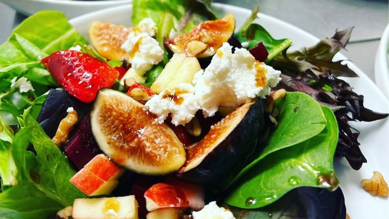 Close up image of a salad with leafy greens, figs, and goat cheese