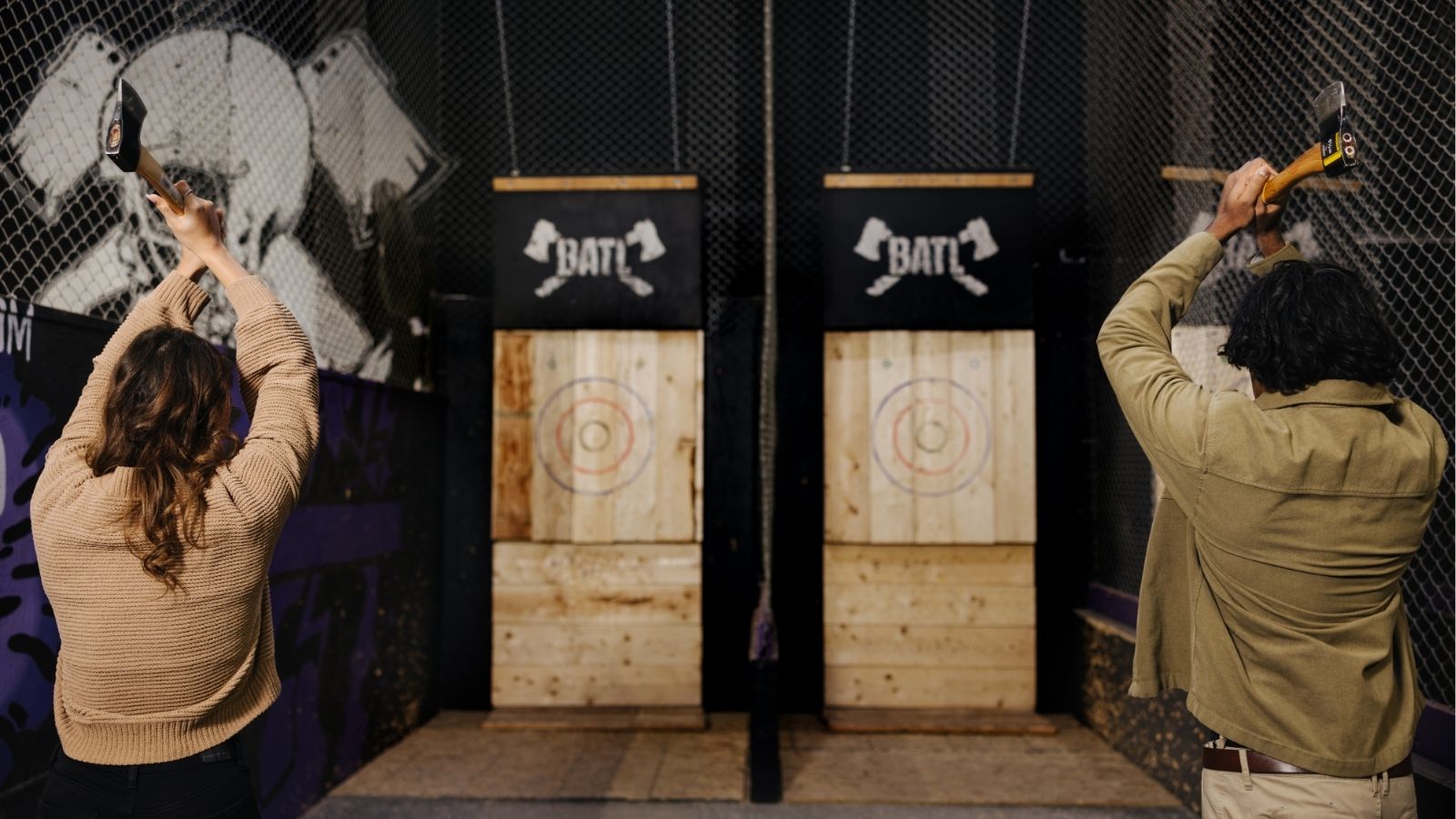 Image of two people from behind getting ready to throw axes at targets at an indoor axe throwing range