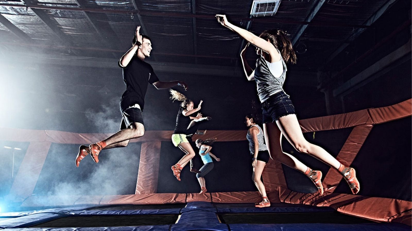 Image of an indoor trampoline park with several people in all different stages of jumping
