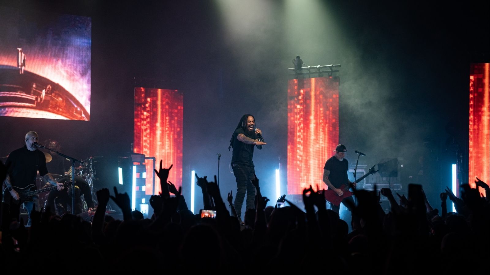 Image of a band on stage performing to a crowd with their hands in the air 