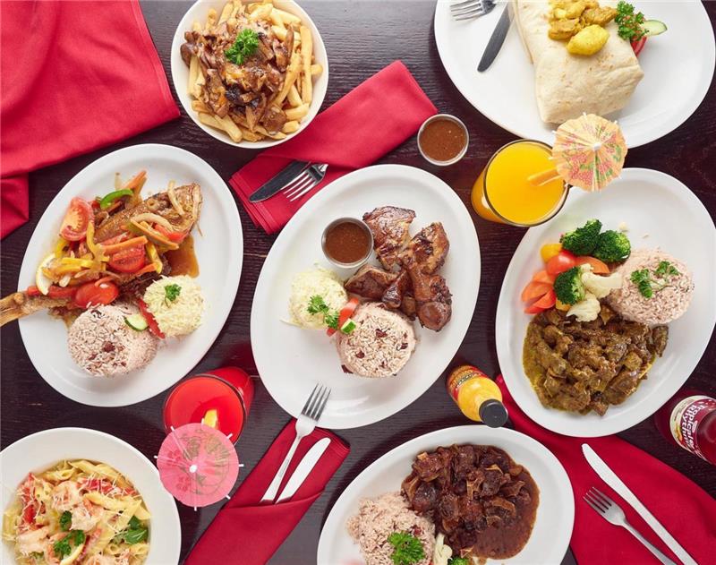 A table with plates full of Jamaican food and tropical drinks