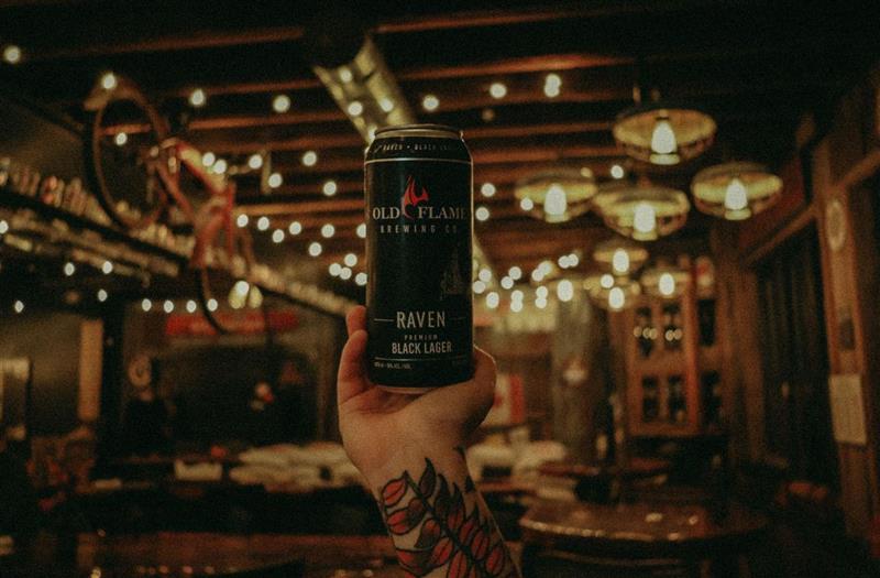 A hand holding up a pint of beer with a beautiful brewery interior behind it