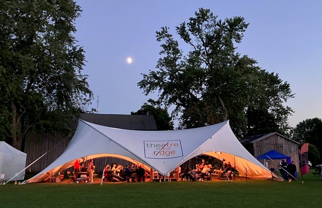 Audience watching a performance in a tent at dusk at Theatre on the Ridge