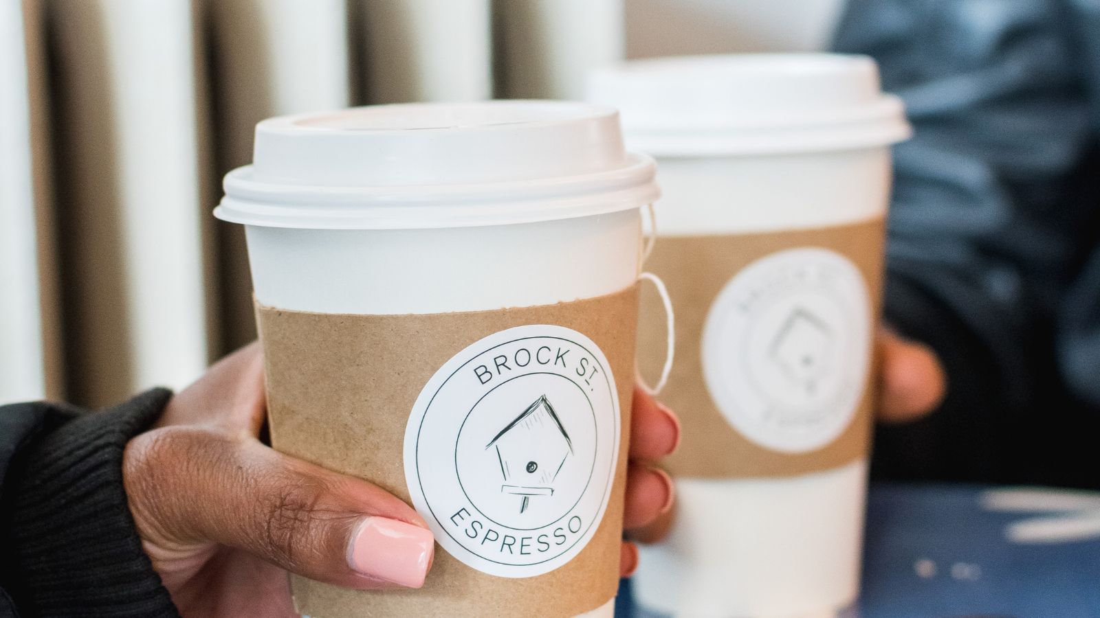 Two sets of hands each holding a cup of coffee from Brock Street Espresso in Whitby, Ontario
