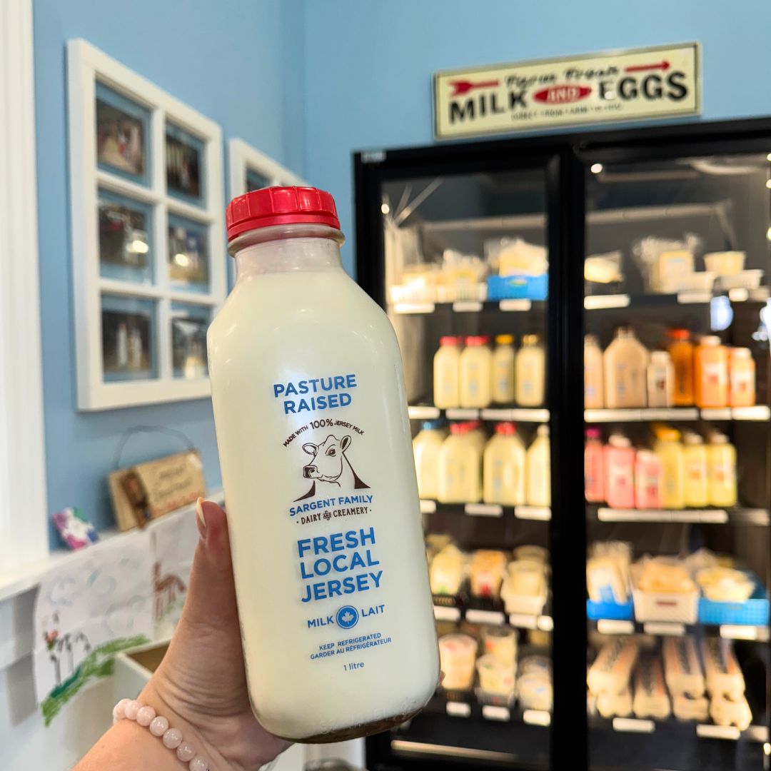 Image of a person holding a glass bottle of milk in front of fridge full of bottles in a farm store