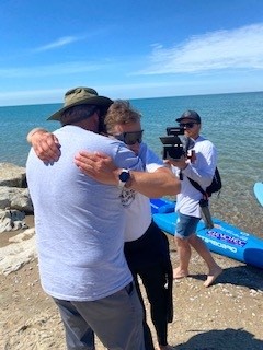 Mike Shoreman receives a hug from a man on shore with a camera behind them