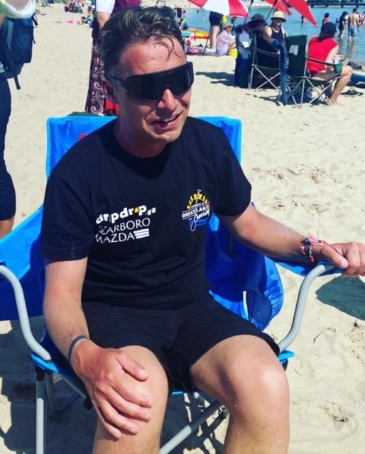 Mike Shoreman sitting in a chair on shore wearing black sunglasses and a black t-shirt