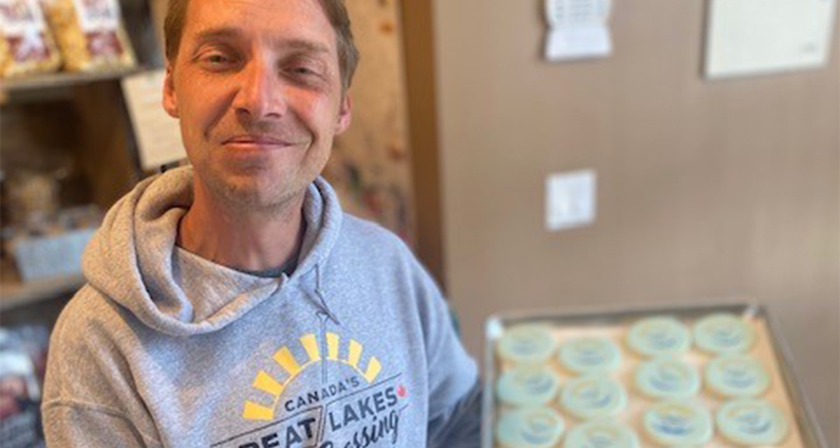 Mike Shoreman holding a tray of cookies wearing a grey Canada's Great Lakes Crossing sweatshirt.
