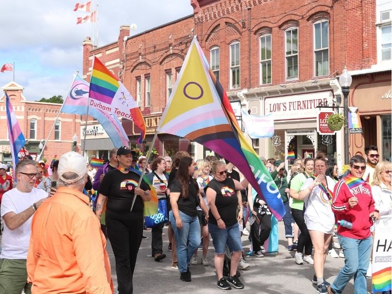 A parade celebrating Pride walking down the main street of a small town with flags and banners