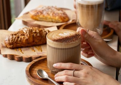 Hand holding a specialty latte with a croissant and desserts from Kareza Cafe in Oshawa, Ontario
