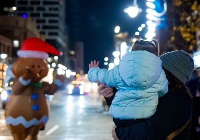 Child waving at a person in a gingerbread man costume at the Santa parade in downtown Oshawa, Ontario