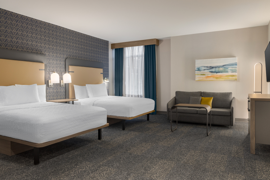 Homewood Suites by Hilton Ajax Hotel guest room with two queen beds, a grey couch and desk