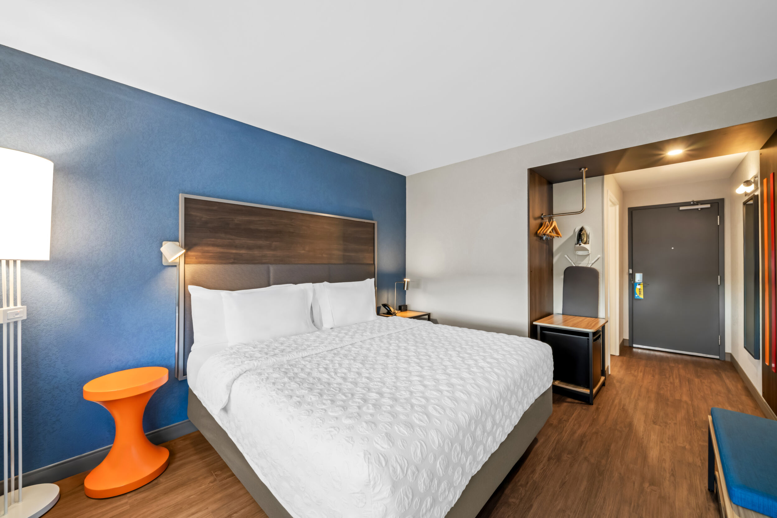 Tru by Hilton Oshawa Hotel guest room with king bed, mini fridge, ironing board and orange side table