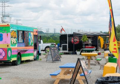 Image of two food trucks parked on the edge of a gravel parking lot with lots of picnic tables between them