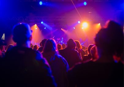 Image of the audience at a concert from behind with lights illuminating the stage
