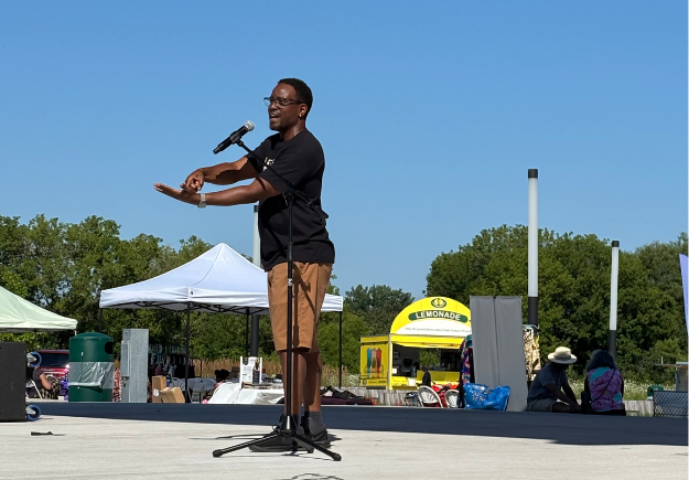 A person standing on stage, speaking into a microphone.