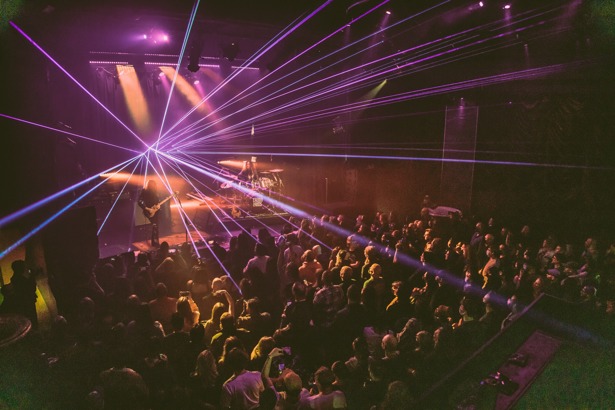 A band playing on stage at the Biltmore Theatre with purple beams of lights.