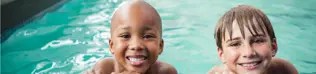 Two boys smiling at the side of a public pool