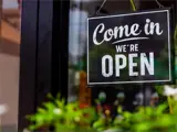 A sign in a window with greenery out front reads Come in we're open.