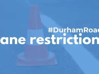 A pylon on a road with a light blue filter over it and white text reading #DurhamRoads Lane restrictions