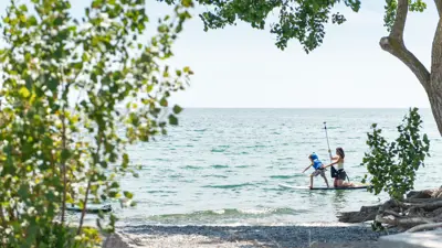 Mother and child on a paddle board along the lake shore.