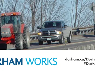 Image of a car and farm equipment driving along a road with text saying, “Durham Works, durham.ca/DurhamWorks #DurhamWorks.”