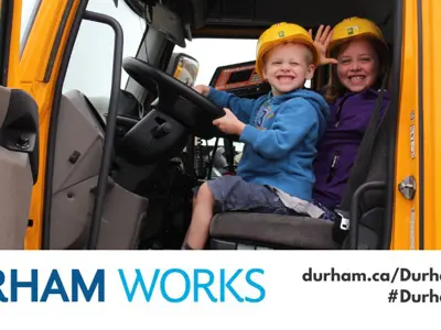 An image of children sitting in a truck with yellow hard hats smiling. Text below reads "Durham Works durham.ca/DurhamWorks #DurhamWorks"