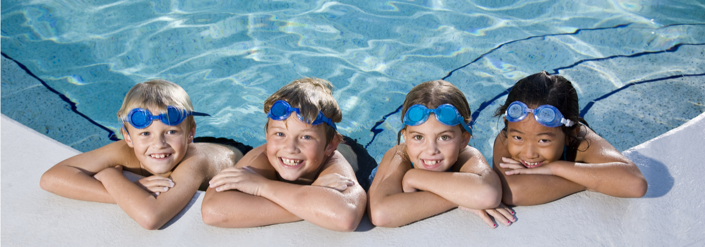 Group of kids smiling at the edge of a public pool